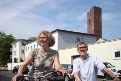 zwei Radfahrerinnen vor dem Schornstein der Einschornsteinsiedlung