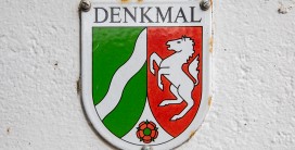 Emailleschild mit Wappen auf weiß gestrichener Wand