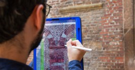 Person mit einem Tablet vor einem Mauerwerk