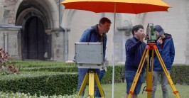 Vermessungsingenieur und Schüler mit einem ELTA, im Hintergrund der Seiteneingang zu einer Kirche