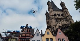 Drohne in der Luft vor mehreren spitzgiebeligen Häusern und einer angrenzenden Kirche
