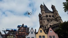 Drohne in der Luft vor mehreren spitzgiebeligen Häusern und einer angrenzenden Kirche