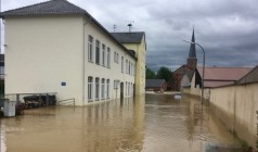 Ein Ort ist überflutet. Vorne sieht man ein Haus, dem das Wasser bis zu den Fenstern steht, im Hintergrund einen Kirchturm.