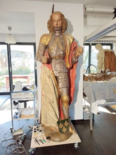 Figur eines Heiligen in Ritterrüstung und Umhang, auf einem Rollwagen in einer Restaurierungswerkstatt postiert