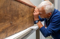 Mann schaut durch eine Lupe auf die Holzwand eines Reliquienkastens
