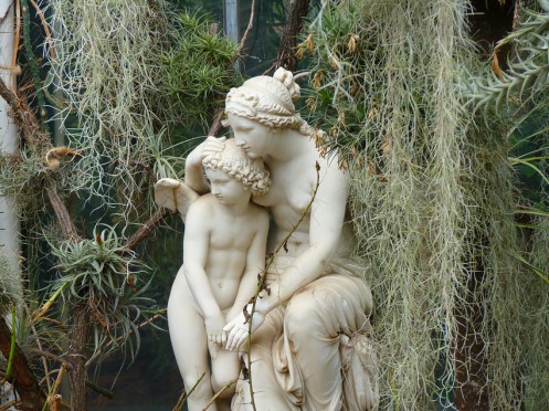 Detailansicht der Statuengruppe einer Venus, die fürsorglich ihren Arm um den kleinen Amor legt, umgeben von Pflanzen