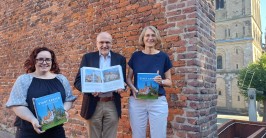 drei Personen mit der Publikation in den Händen vor einer Mauer, im Hintergrund ein Teil des Xantener Doms