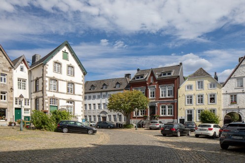 ein kopfsteingepflasterter Platz mit parkenden Autos, umgeben von alten Hausfassaden