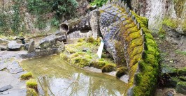monumentale Drachenskulptur mit abgebrochenem Kopf an einem Teich