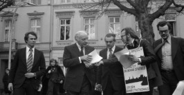 mehrere Männer im Gespräch mit einem Demonstranten, der ein Schild umgehängt trägt