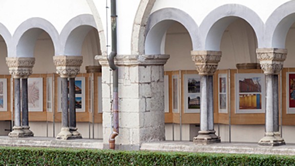 Durchblick durch die Bögen des romanischen Kreuzganges der Abtei Brauweiler auf eine Fotoausstellung zum Thema "Farbe!"